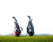 Two golf bags—red/black and black—standing on grassy hill against bright sky.