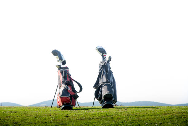 Two golf bags—red/black and black—standing on grassy hill against bright sky.