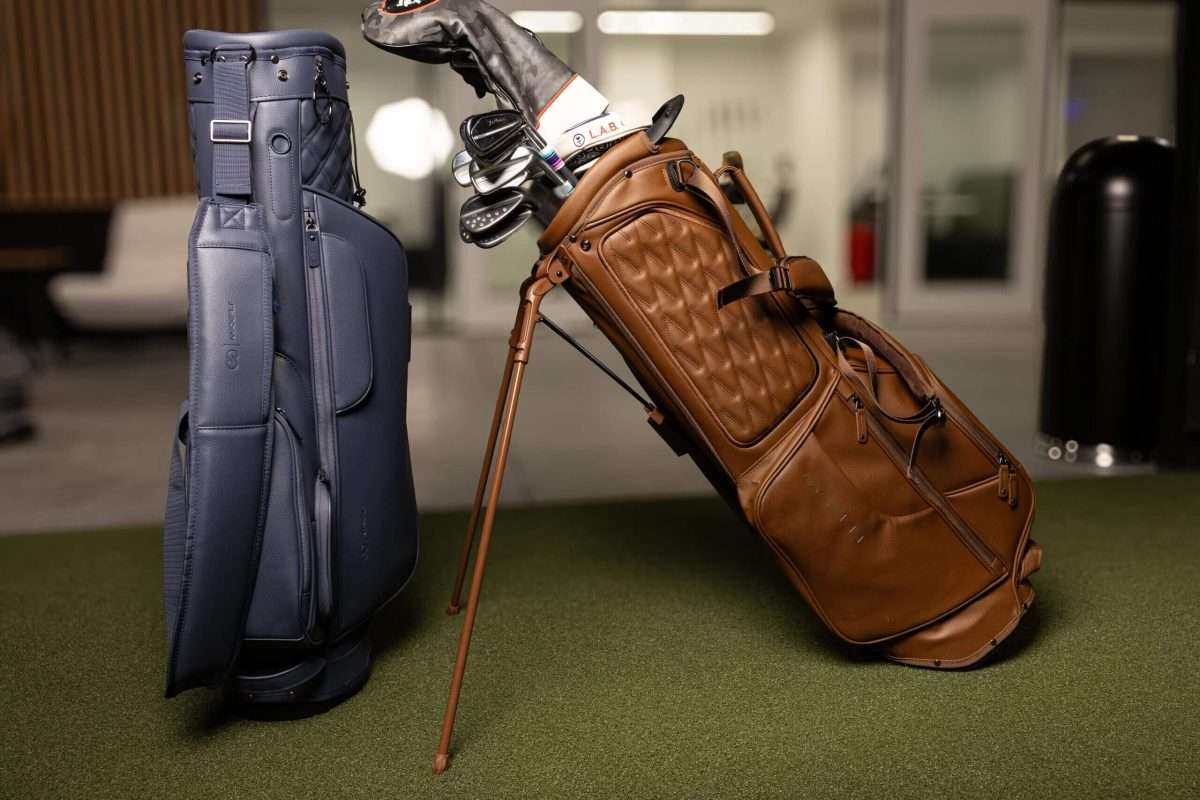 Two premium golf bags, navy and brown leather, with clubs on a green mat.