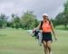 Smiling woman walks on the golf course, carrying her Golf Bag and clubs.