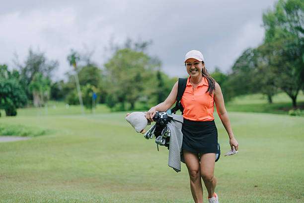 Smiling woman walks on the golf course, carrying her Golf Bag and clubs.