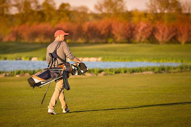 Man walking on golf course with a stand golf bag over his shoulder at sunset.
