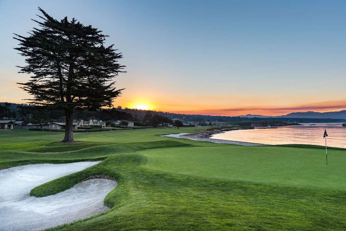 Picturesque golf course sunset over ocean with cypress tree and sand trap. Add your golf bag.