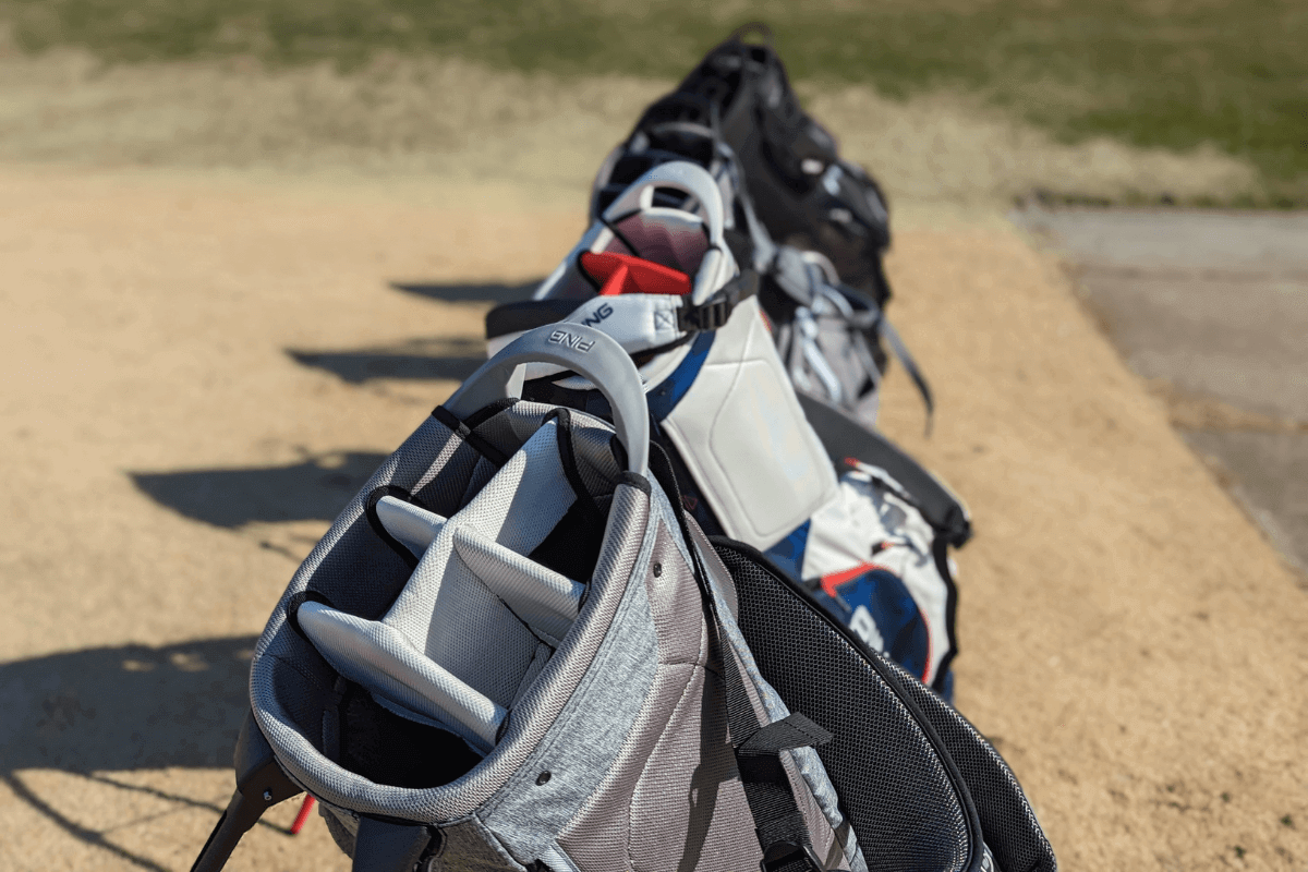 Row of gray and white golf bags on a practice range, ready for use.