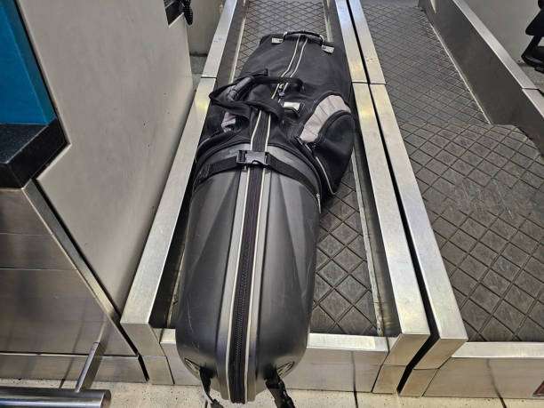 Black hard-shell travel golf bag case on an airport baggage conveyor belt.