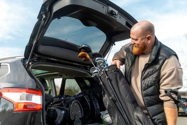 Man with beard removing a black golf bag from his car's trunk.