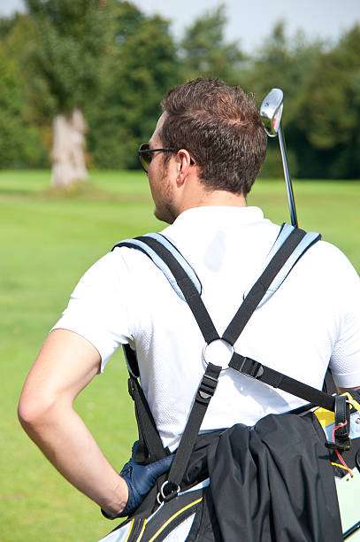 Man on a golf course carrying a white and black golf bag with comfortable straps.