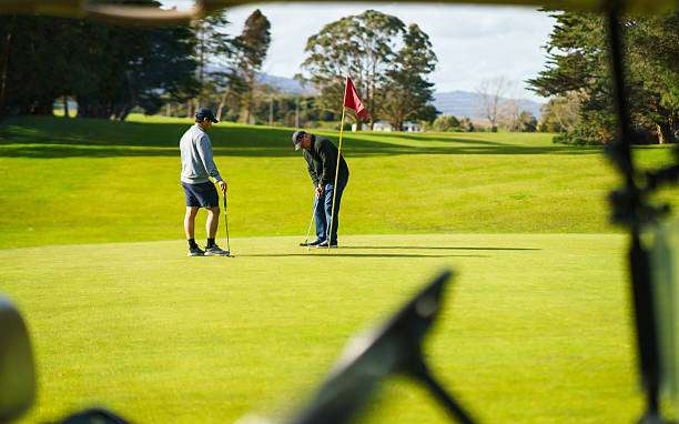 Two golfers putting on the green, likely with their golf bag nearby in the cart.