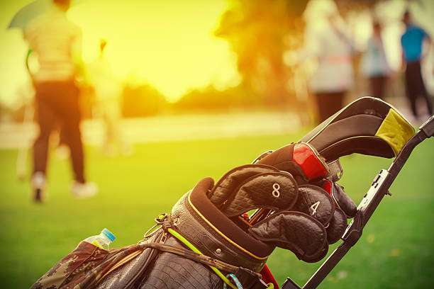 Golf clubs with headcovers in a classic golf bag on a pushcart at sunset.
